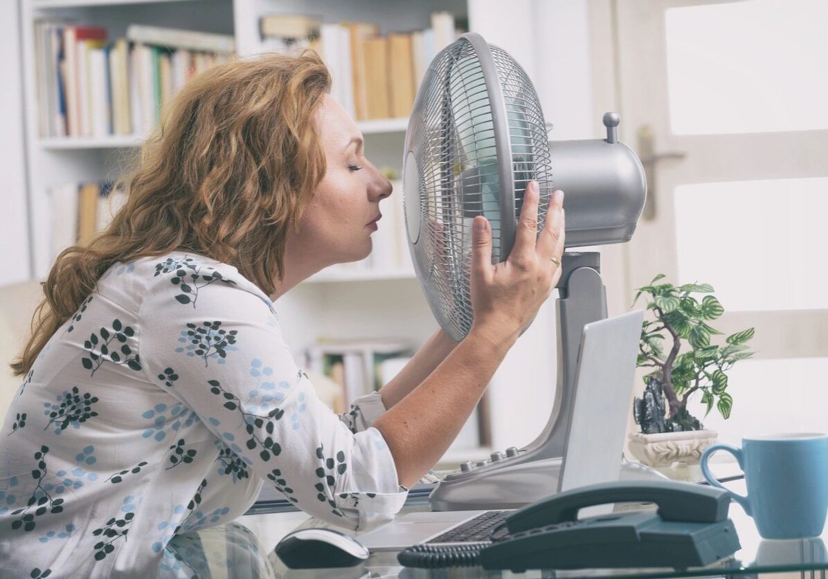 Woman cooling off with fan during hot weather